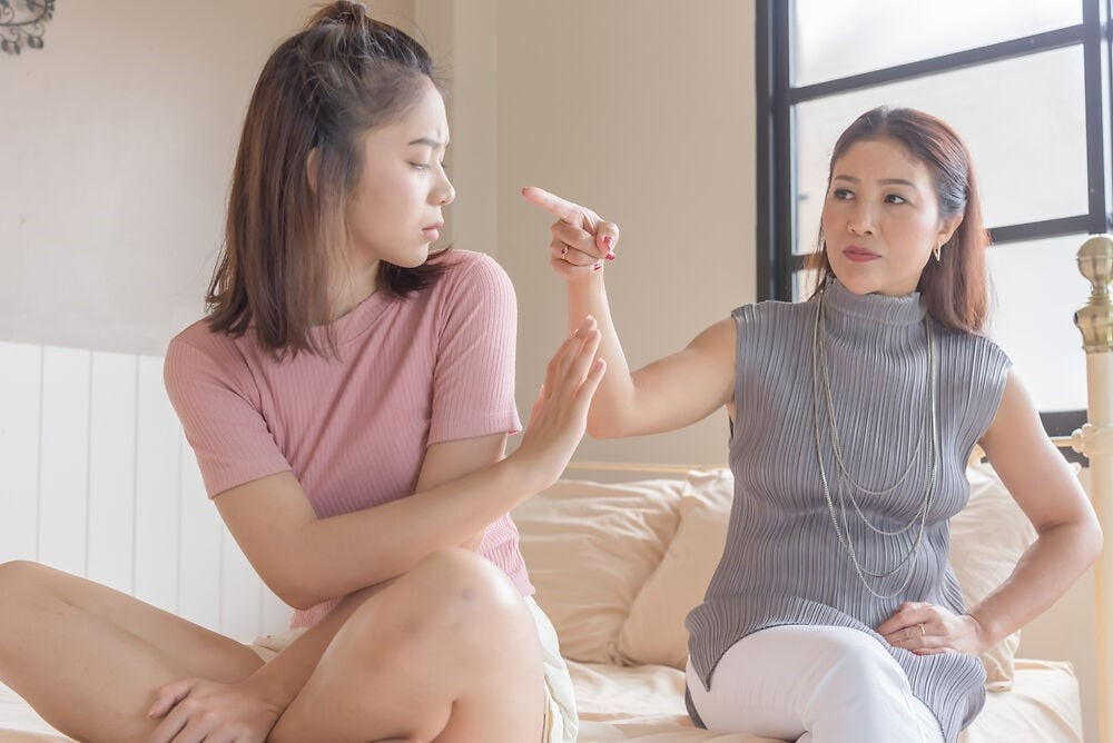 Alt text: Người mẹ có vẻ mặt khó chịu, ánh mắt nhìn xa xăm, trong khi cô con gái tuổi dậy thì quay lưng lại, thể hiện sự xung đột và căng thẳng trong giao tiếp giữa mẹ và con.